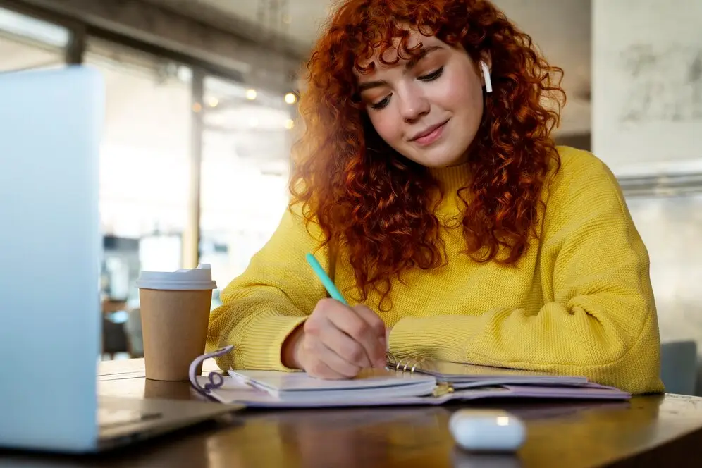 Femme buvant du chocolat chaud dans un café, tout en suivant ses cours en ligne sur son ordinateur portable.