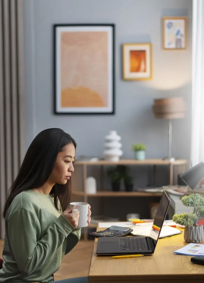 Femme travaillant depuis chez elle, concentrée et utilisant son ordinateur portable dans un environnement de bureau à domicile.