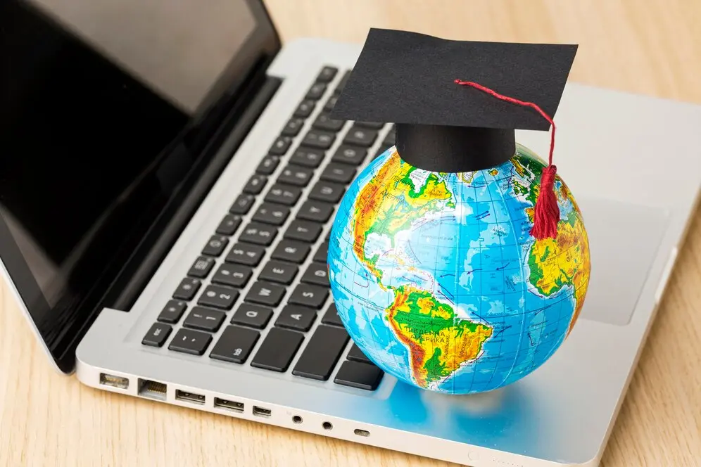 Globe terrestre avec un chapeau de diplômé posé sur un ordinateur portable, symbolisant l'éducation en ligne internationale
