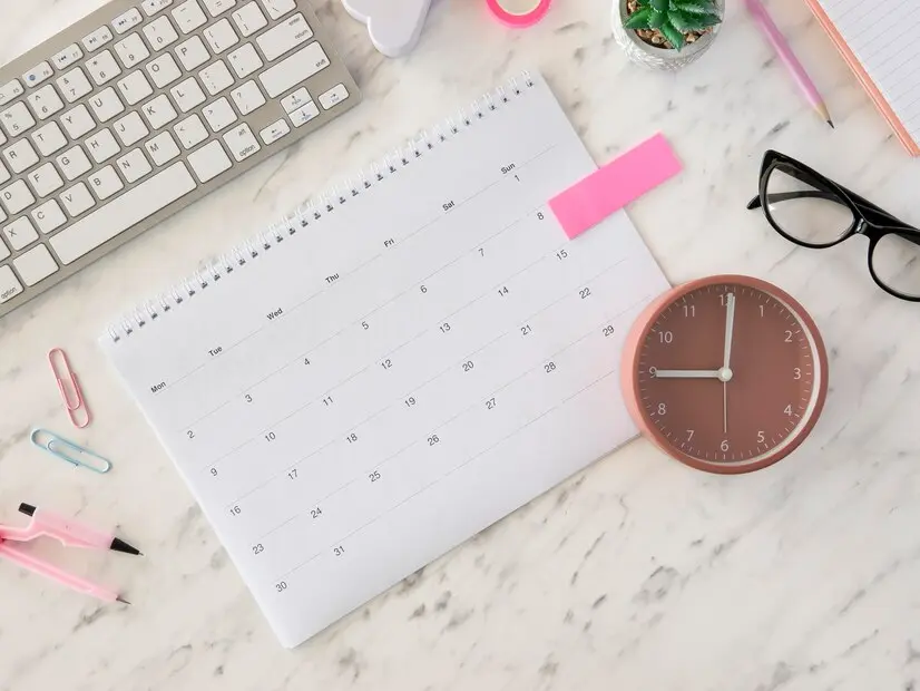 Calendrier et horloge posés sur un bureau plat, représentant l'organisation et la gestion du temps.