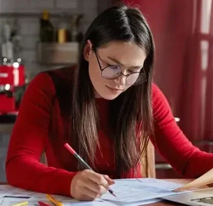 Femme concentrée sur la planification et l'analyse de statistiques, assise à son bureau dans une cuisine, travaillant sur des recherches pour sa société.