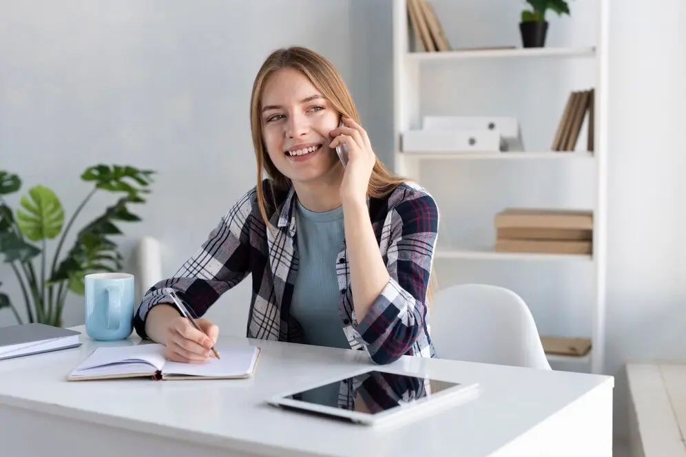 Femme souriante parlant au téléphone depuis son bureau, engagée dans une conversation professionnelle