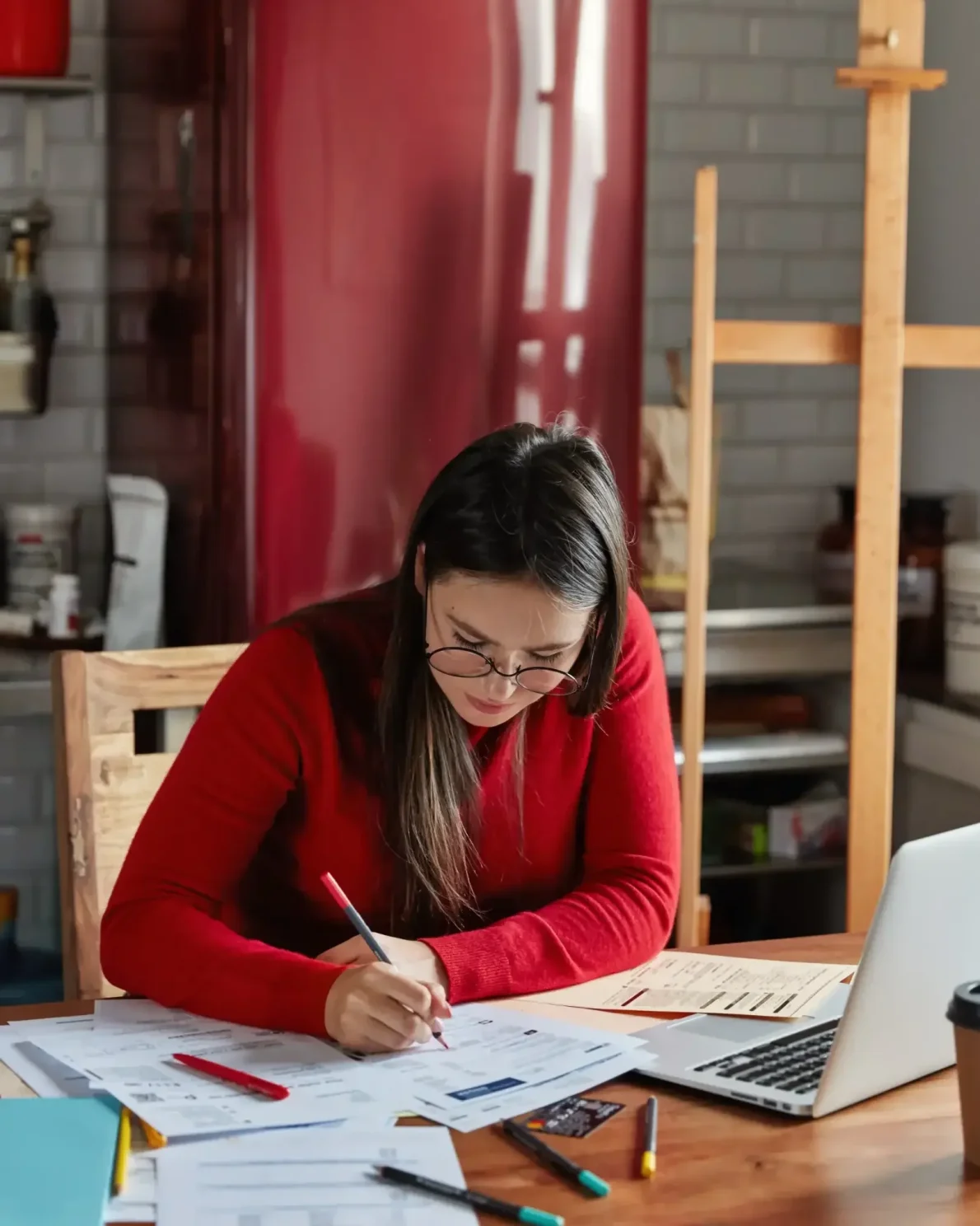Femme travaillant sur un rapport financier dans une cuisine, avec un réfrigérateur en arrière-plan.