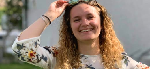 Étudiante souriante portant des lunettes de soleil, rayonnante et détendue.