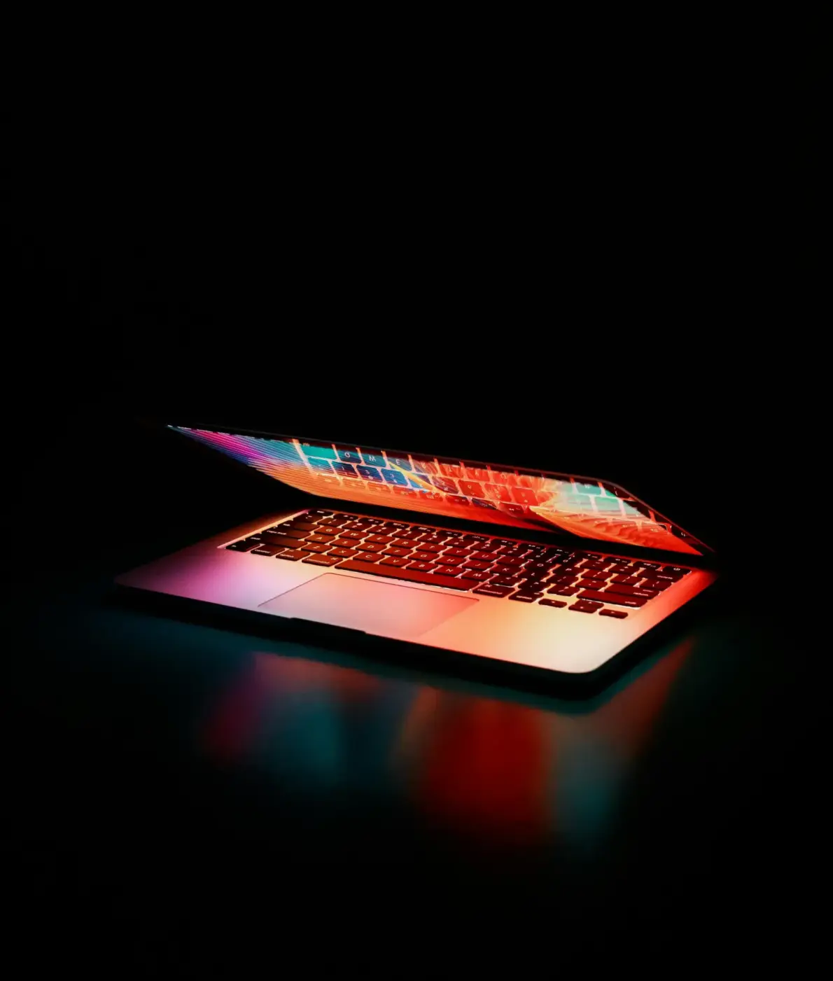 Ordinateur portable partiellement ouvert avec des lumières colorées se reflétant sur le clavier et l'écran, dans une ambiance sombre et moderne.
