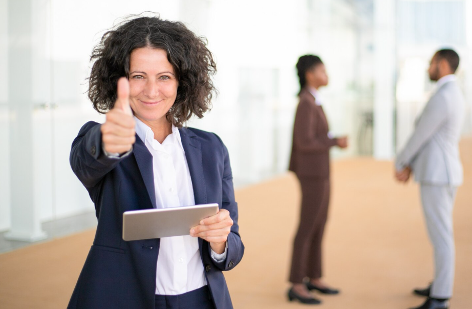Apprenante satisfaite tenant une tablette et levant le pouce après une formation à distance réussie